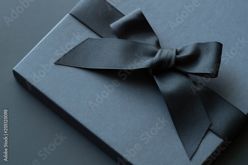 Black gift box on a dark contrasted background, decorated with a textured bow and feathers, creating a romantic atmosphere. Typically used for birthday, anniversary presents, gift cards, post cards.