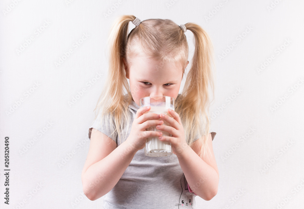 young cute little blonde girl in light grey t-shirt smiling and holding glass of milk young cute little blonde girl in light grey t-shirt smiling and holding glass of milk