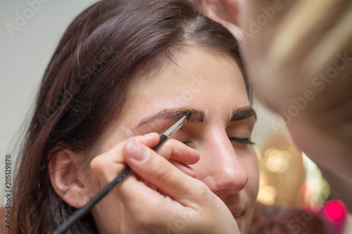 Beautiful young woman gets eyebrow correction procedure. Young woman painting her eyebrows in beauty saloon. close-up of a young woman plucking eyebrows with tweezers