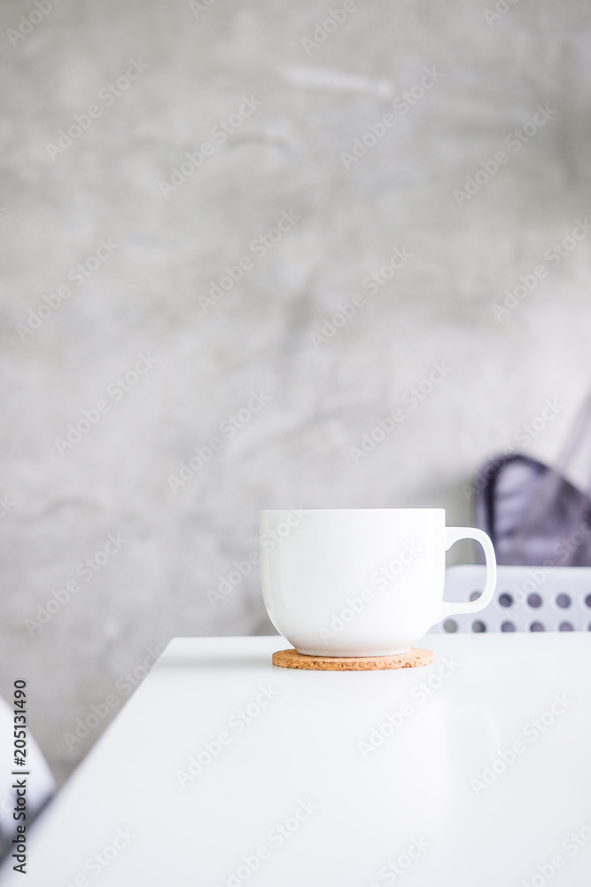 White cup on white table against light gray concrete wall. Minimalism concept. Layout, copyspace for text