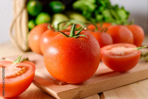 Close-up of fresh, ripe tomatoes with vegetables on wooden background.
