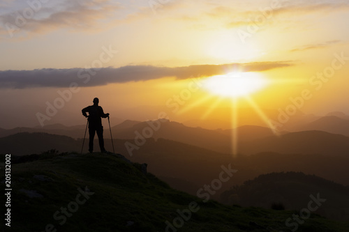 Hiker on the top of a mountain facing the sun.