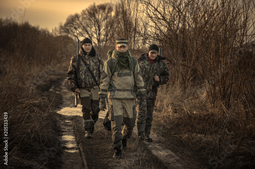 Group of men hunters with hunting equipment going on rural road hunting season sunset