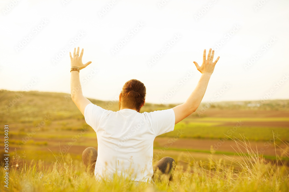 Man sitting on field and raising arms up at sunset Man sitting on field and raising arms up at sunset