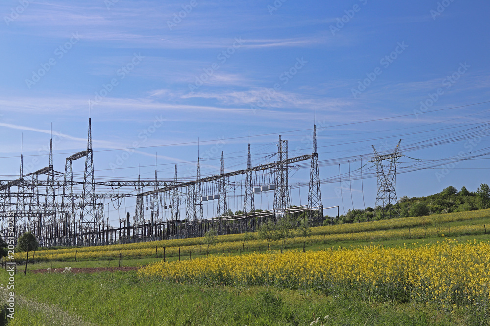 High voltage electric lines cross the hilly mestnost. Electric station in the summer under the open sky. Power industry. Ecology of nature. Metal technological structures. Strategic object at a field.