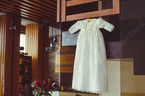 christening baby dress. Close-up of a cute newborn baby dress. Stylish embroidered white dress in a cozy interior. Concept childhood education and fashion
