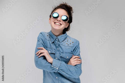 Young brunette girl in round glasses. Hairs are gathered in a bun. The girl folded her arms. photo