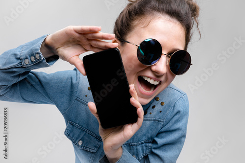 Young brunette girl in round glasses. Hairs are gathered in a bun. Girl with a black phone. photo