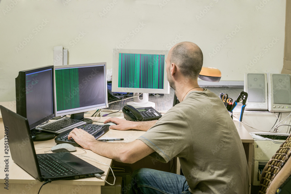 The workplace of the system administrator. The programmer develops software. A specialist sits at a table with a lot of monitors and a laptop.