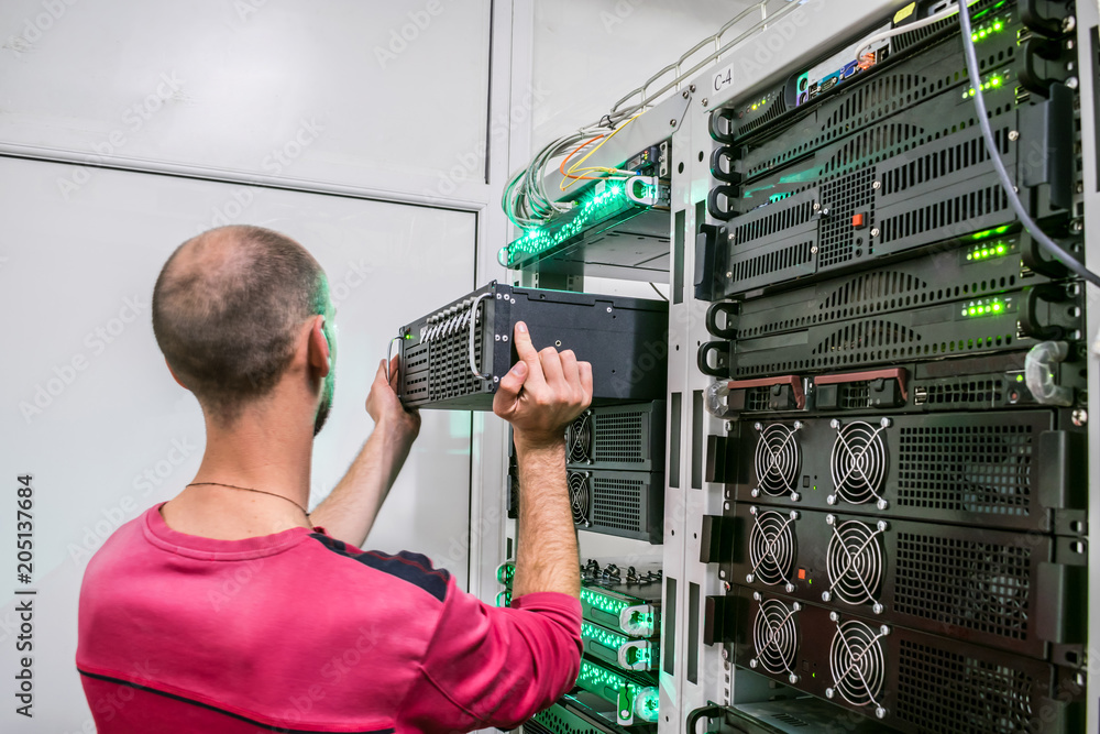 Technical Support Engineer performs the installation of a new server in a  rack with computer equipment. The man is working in the server room of the  data center Photos | Adobe Stock