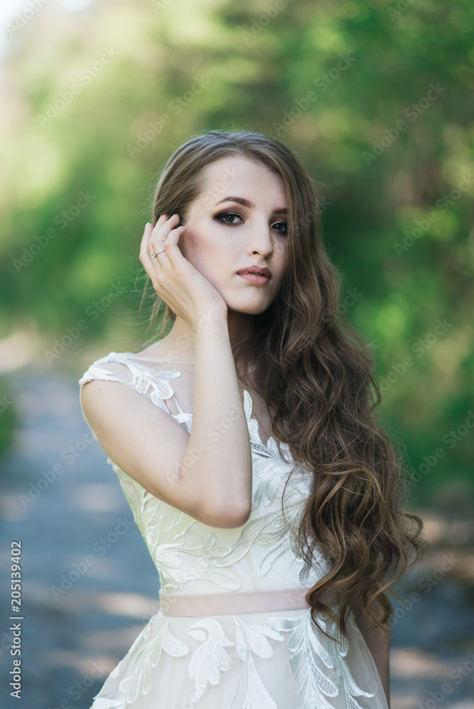 Beautiful brunette bride with curls, makeup and stylish dress. Portrait on the background of green trees. Summer wedding day. Beautiful brunette bride with curls, makeup and stylish dress. Portrait on the background of green trees. Summer wedding day.