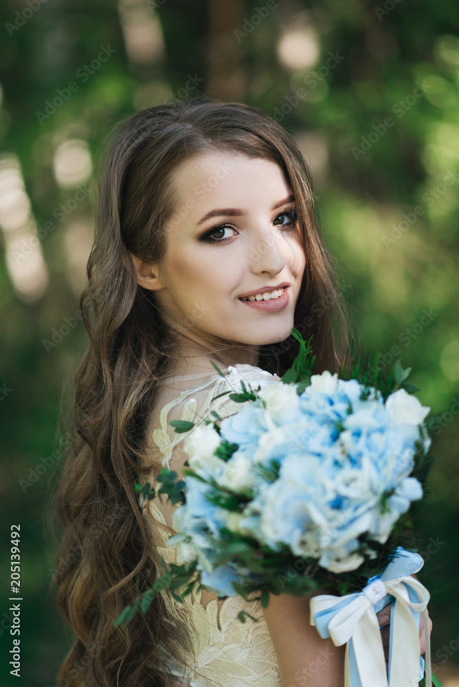 Beautiful brunette bride with curls, makeup and stylish dress. Portrait on the background of green trees. Summer wedding day. Beautiful brunette bride with curls, makeup and stylish dress. Portrait on the background of green trees. Summer wedding day.