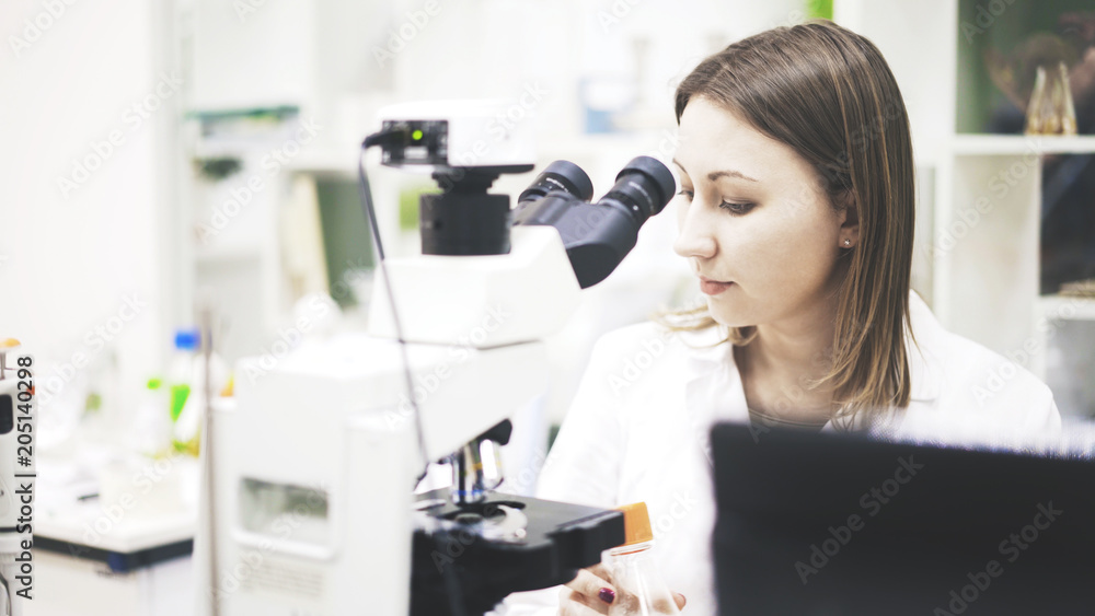 A young woman doctor is sitting in front of the microscope. A doctor is working in the laboratory in front of the microscope, holding a sample of medicine. A young woman doctor is sitting in front of the microscope. A doctor is working in the laboratory in front of the microscope, holding a sample of medicine.
