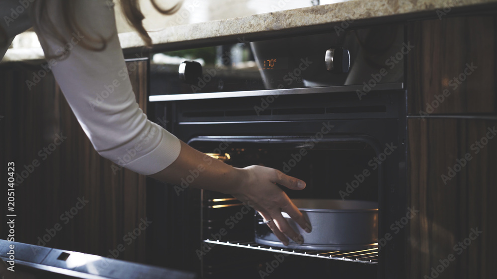A woman without a glove puts a container into an oven in the kitchen