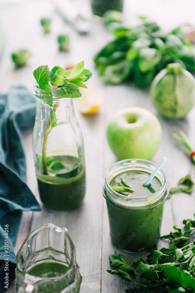 Green smoothie in bottle and in mason jars with apple,baby spinach, parsley and banana, on a wooden board against a dark background Green smoothie in bottle and in mason jars with apple,baby spinach, parsley and banana, on a wooden board against a dark background