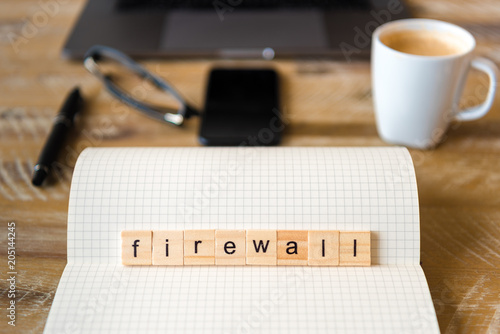 Closeup on notebook over wood table background, focus on wooden blocks with letters making Firewall word