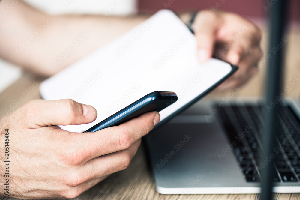 close-up partial view of person holding notebook and using smartphone close-up partial view of person holding notebook and using smartphone