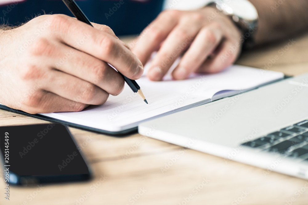 cropped shot of person writing in notebook at wooden table cropped shot of person writing in notebook at wooden table
