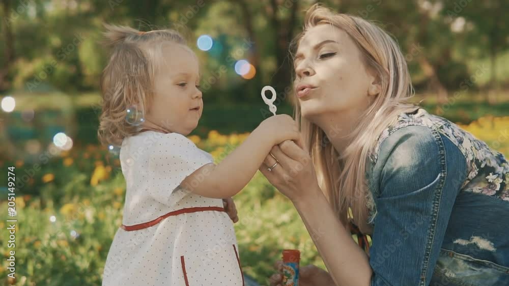 Happy Mother and Little Daughter playing together, blowing soap bubbles. Beauty Mum and Child in Park. Family, Mother's Day Joy. Happy Family Concept in slow motion Happy Mother and Little Daughter playing together, blowing soap bubbles. Beauty Mum and Child in Park. Family, Mother's Day Joy. Happy Family Concept in slow motion