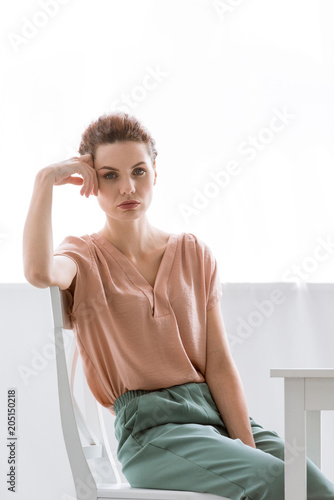 depressed young woman sitting on chair at home and looking at camera