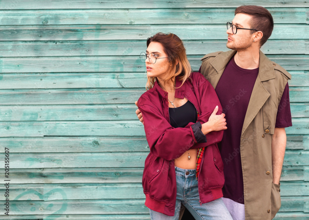 fashion couple in their glasses with burgundy clothes posing on a blue wooden wall fashion couple in their glasses with burgundy clothes posing on a blue wooden wall