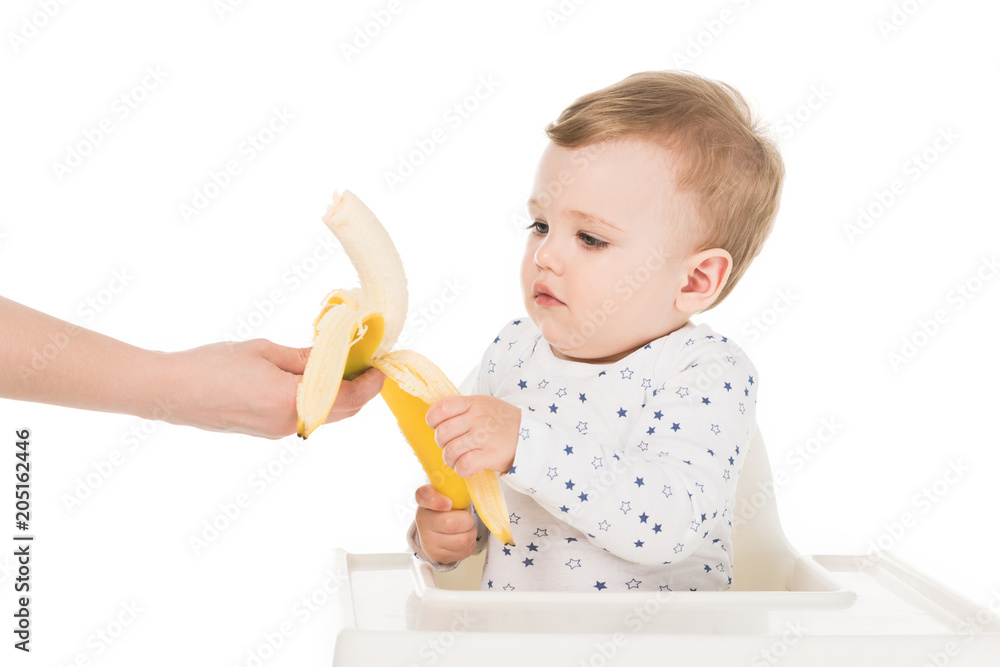 cropped shot of mother giving banana to son in highchair isolated on white background cropped shot of mother giving banana to son in highchair isolated on white background
