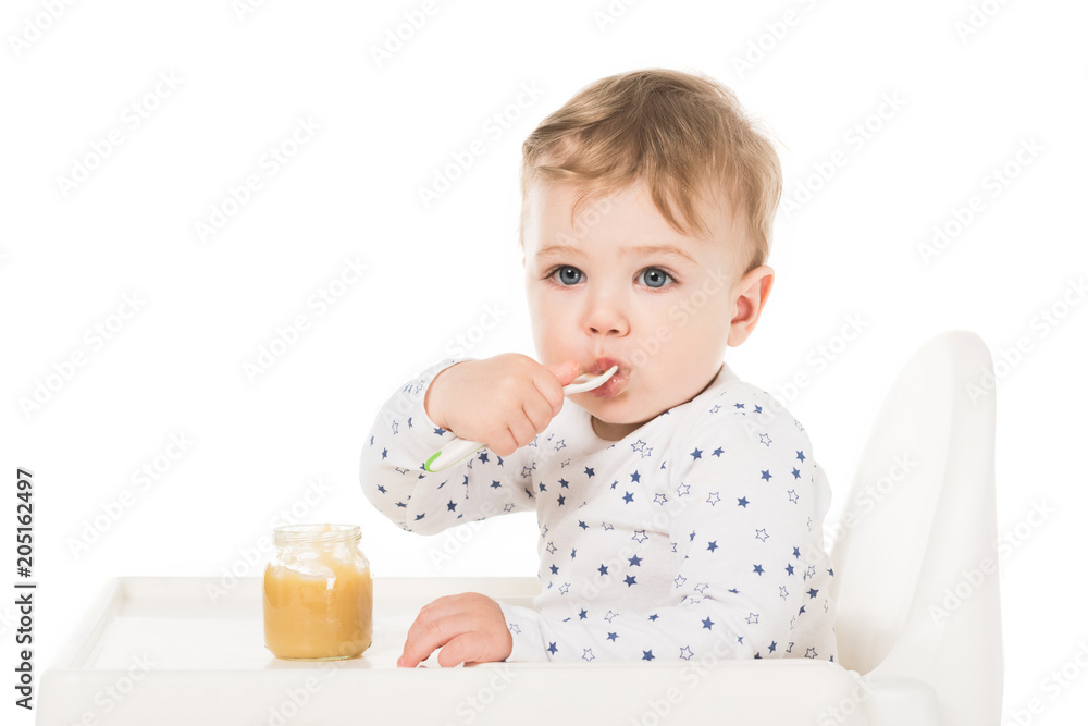 adorable baby boy eating puree from jar and sitting in highchair isolated on white background adorable baby boy eating puree from jar and sitting in highchair isolated on white background