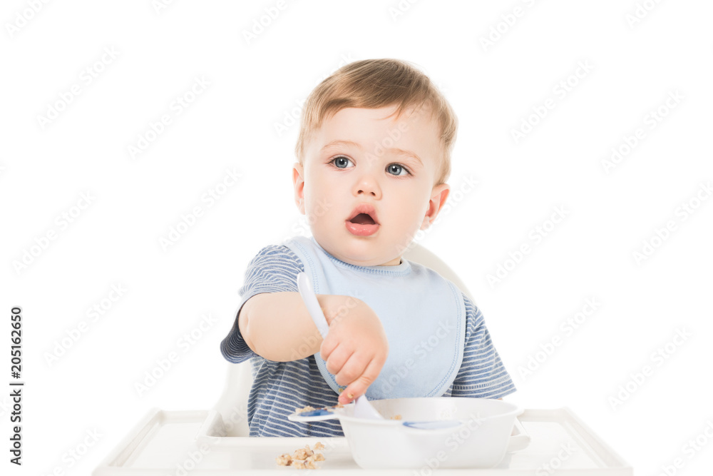 adorable little boy in bib sitting in highchair and eating by spoon isolated on white background adorable little boy in bib sitting in highchair and eating by spoon isolated on white background