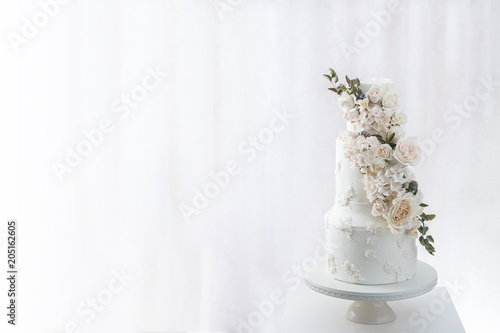 Fotografie White tiered wedding cake with edible bouquet of flowers wrapped around it