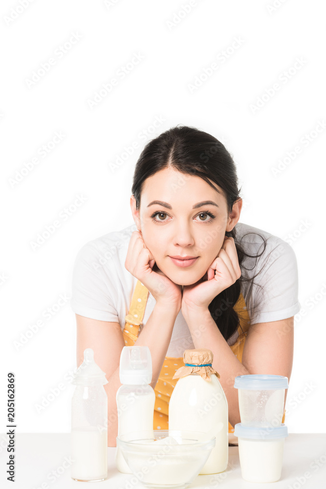 young woman in apron standing at table with milk, bowl, plastic containers and baby bottles young woman in apron standing at table with milk, bowl, plastic containers and baby bottles