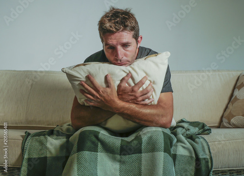 young sad and desperate man at home sitting at sofa couch holding pillow suffering depression and stress worried about problem feeling miserable