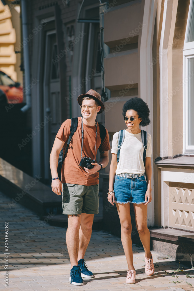 interracial couple of young tourists with camera walking on street