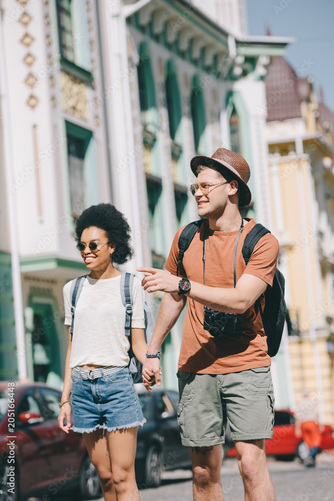 Fototapeta premium young male tourist with camera pointing by finger to girlfriend walking near