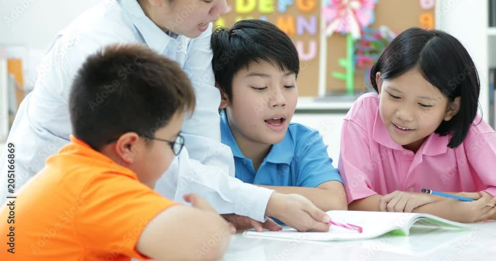 Young asian teacher helps young school kids in class, close up