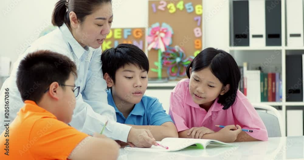 Young asian teacher helps young school kids in class, close up Young asian teacher helps young school kids in class, close up