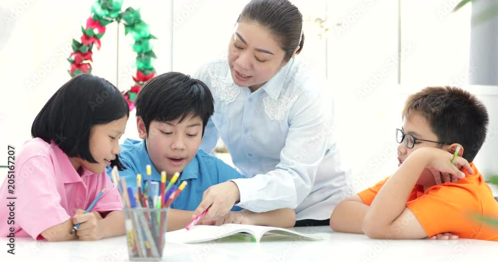 Young asian teacher helps young school kids in class, close up Young asian teacher helps young school kids in class, close up