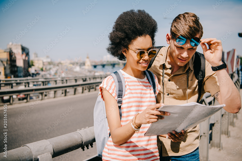 multiethnic young couple of tourists looking at map