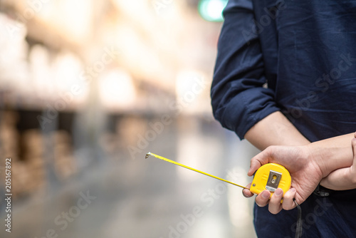 close up of male hand holding yellow tape measure in warehouse. Furniture product design measuring concept