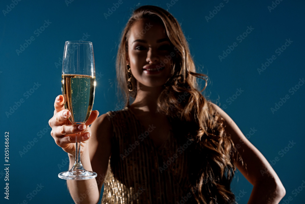 attractive woman showing glass of champagne in evening isolated on blue attractive woman showing glass of champagne in evening isolated on blue