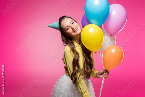 attractive woman posing with party hat and balloons isolated on pink