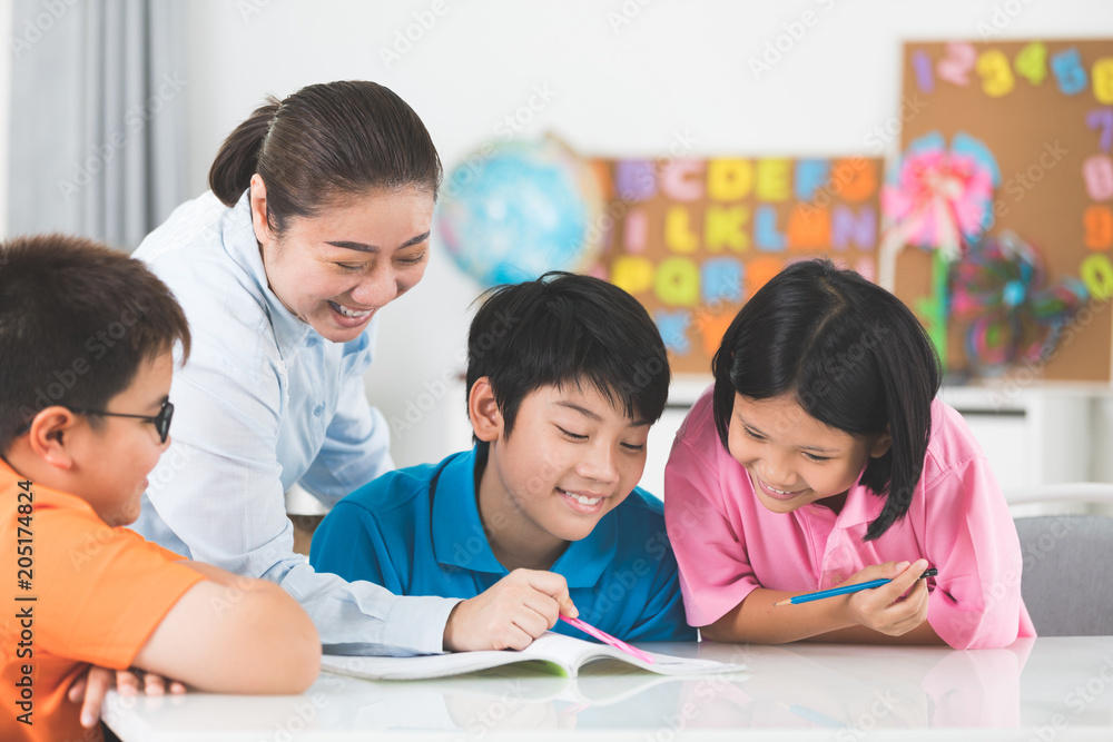 Young asian teacher helps young school kids in class. Young asian teacher helps young school kids in class.
