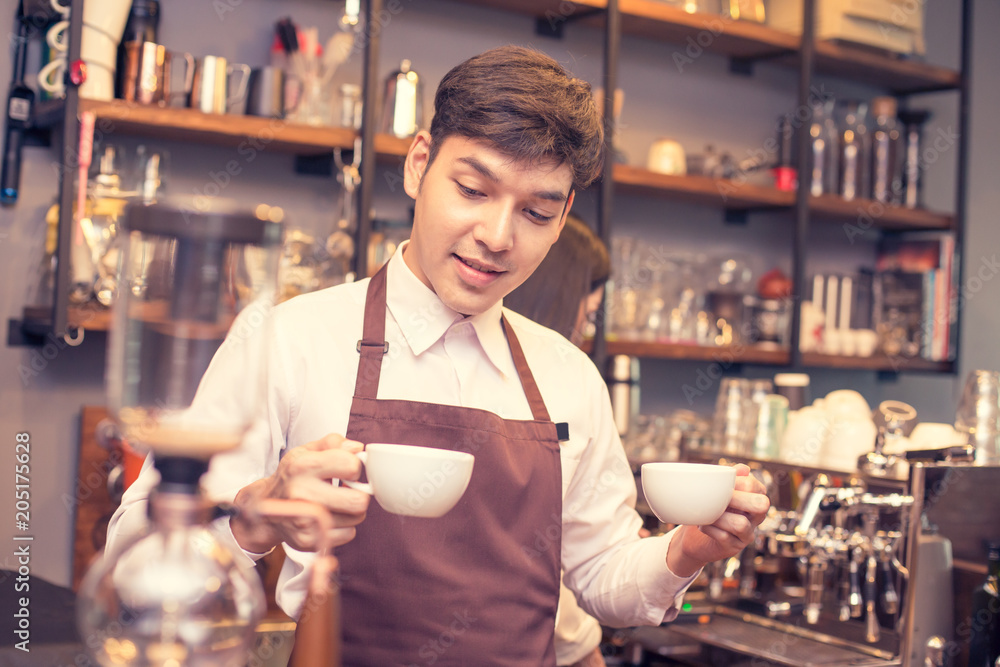 Asian male barista holding coffee cup in coffee shop counter.  Barista male working at cafe. Man working with small business owner or sme concept. Vintage tone.