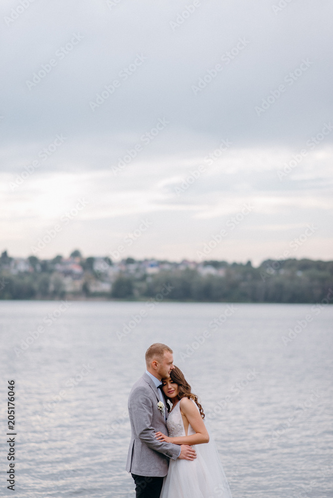 An amazing couple on their wedding day near the lake hug and enjoy each other. The bride and groom with a bouquet are happy together