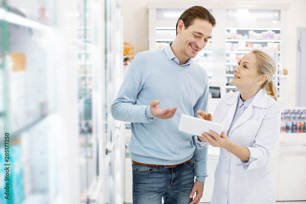On this shelf. Confident female pharmacist using tablet while speaking with man On this shelf. Confident female pharmacist using tablet while speaking with man