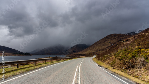 Beautiful countryside road in the Highlands of Scotland, leading towards storm clouds into the distance - typical Scottish landscape with impressive scenery and breathtaking views