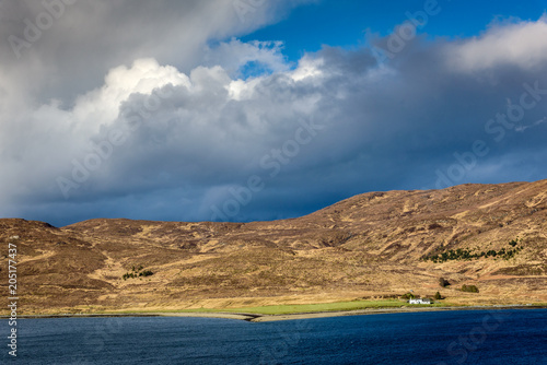 Small white farmhouse in the foot of a beautiful hill on the Isle of Skye in Scotland - impressive scenery under stormy clouds on a bright summer day