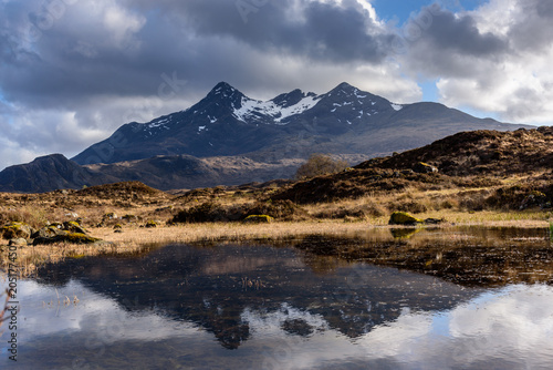 Beautiful reflection of Sgurr nan Gillean in the calm waters of a mountain lake with dramatic clouds hanging over the hill tops © photoenthusiast
