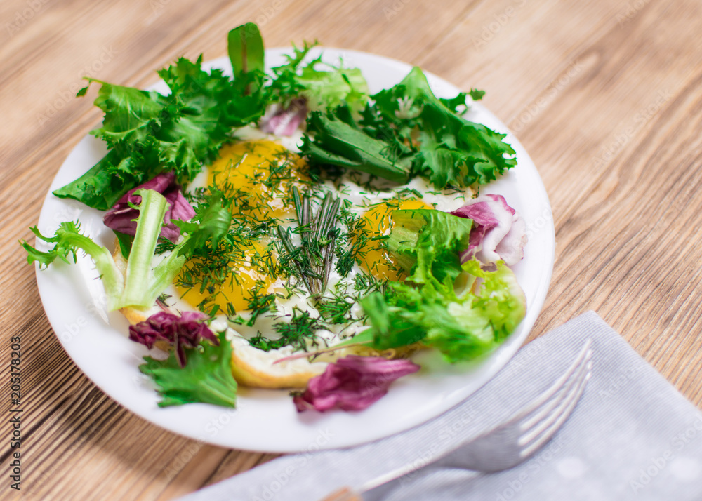 Fried eggs with greens on a plate on a wooden background. Healthy breakfast. Fried eggs with greens on a plate on a wooden background. Healthy breakfast.