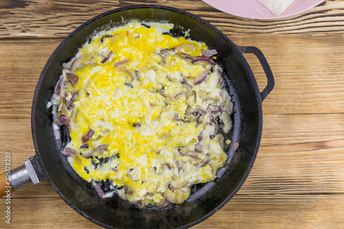 Scrambled eggs with onions in a frying pan on a wooden background.