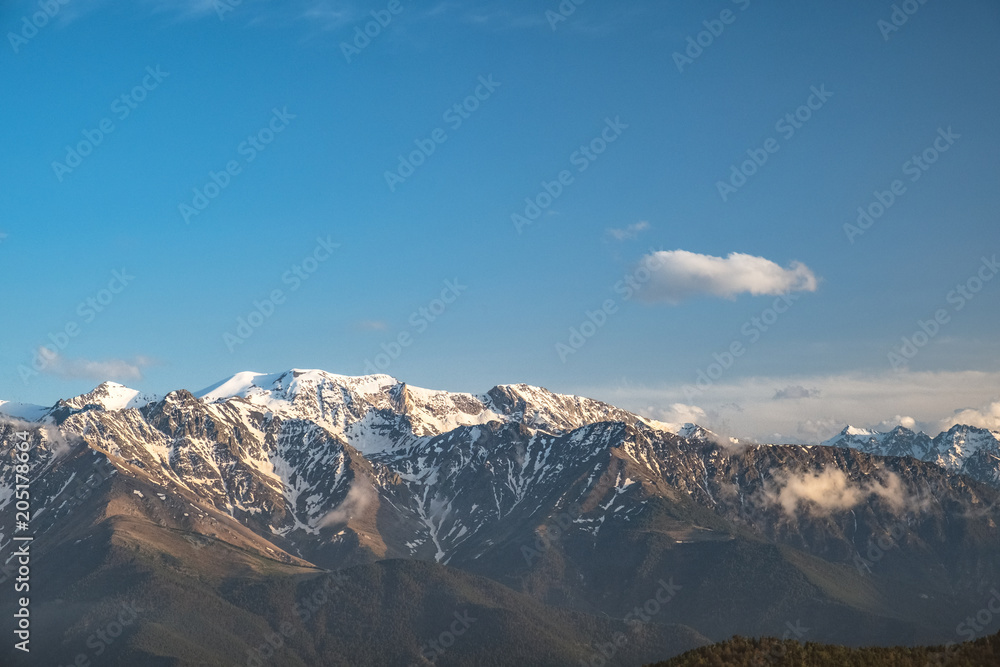 the tops of the mountain ranges snow-covered in the clouds of the Karachay-Cherkess Republic, the Caucasus, in the spring evening the tops of the mountain ranges snow-covered in the clouds of the Karachay-Cherkess Republic, the Caucasus, in the spring evening